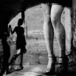 Blue-City Prostitution Line Looks Like a Drive- Thru legs in high heels under an archway with blurred shadow figure