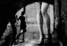 Blue-City Prostitution Line Looks Like a Drive- Thru legs in high heels under an archway with blurred shadow figure