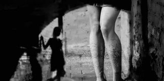 legs in high heels under an archway with blurred shadow figure
