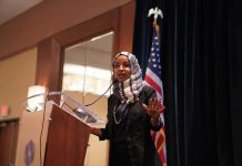 Ilhan Omar’s Troubles Just Got WORSE! Ilhan Omar speaking at a podium with a microphone