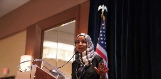Ilhan Omar’s Troubles Just Got WORSE! Ilhan Omar speaking at a podium with a microphone