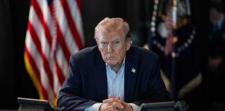Trump Dangles Cash Bounties For Fraud Whistleblowers Donald Trump seated at a table between two desk phones