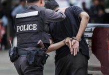 Japan Hands Russian Mastermind Over To Germany Police officer escorting handcuffed man to a vehicle
