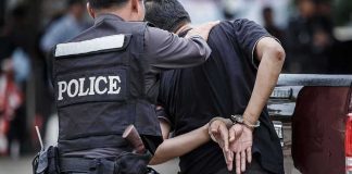 Japan Hands Russian Mastermind Over To Germany Police officer escorting handcuffed man to a vehicle