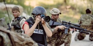 Teddy Williams photographing near armed soldiers in a field